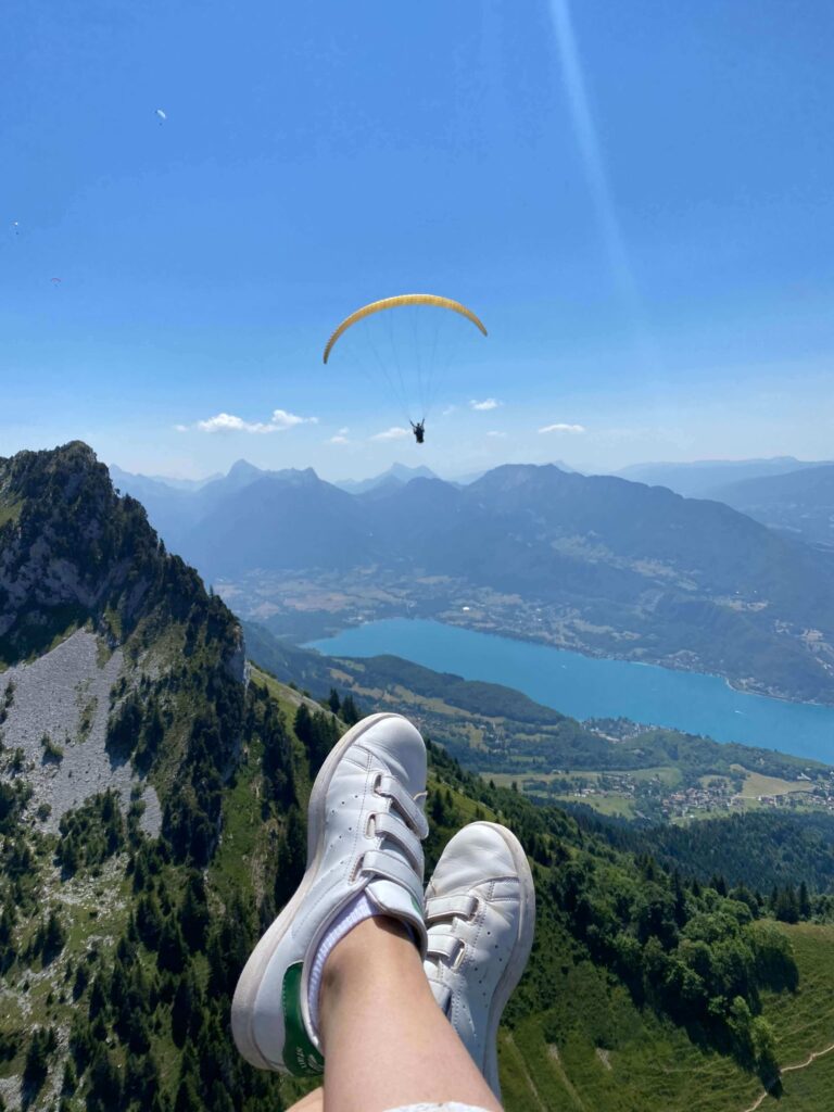 a person's feet in white shoes and a parachute above a mountain